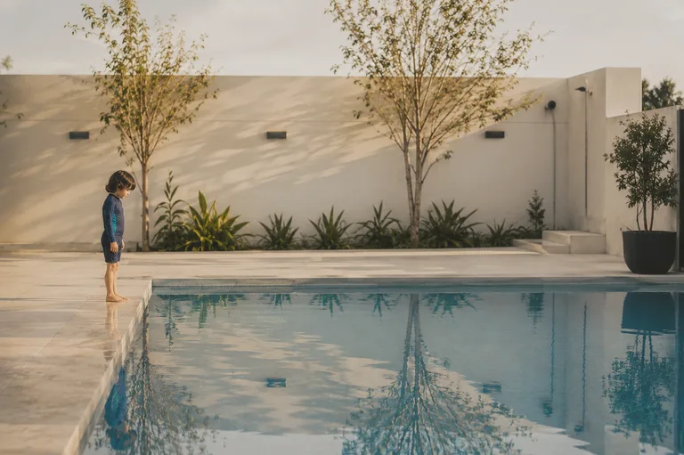 A child standing at the pool edge, looking into the water