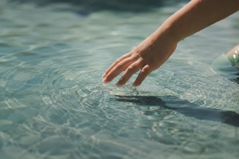 A child's fingers meeting the surface of the water