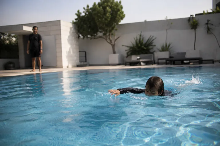 A child swimming independently while a coach watches from a distance
