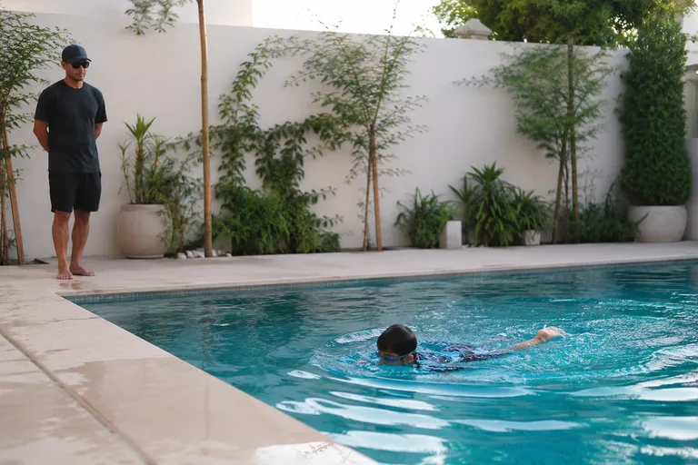 A coach watching a child swim, standing back from the pool edge